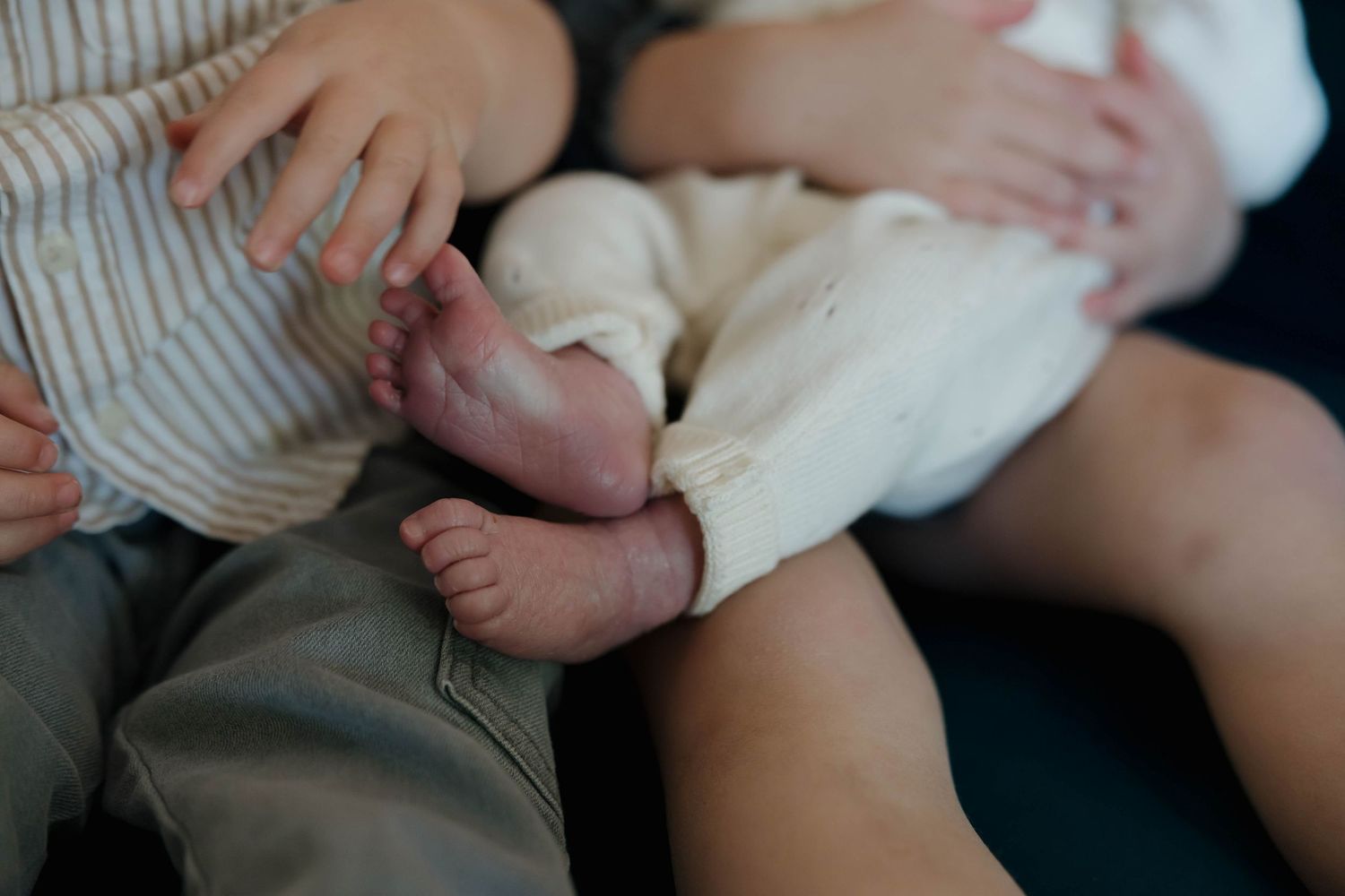 Close-up of tiny newborn baby feet being gently held by adult hands against white background.