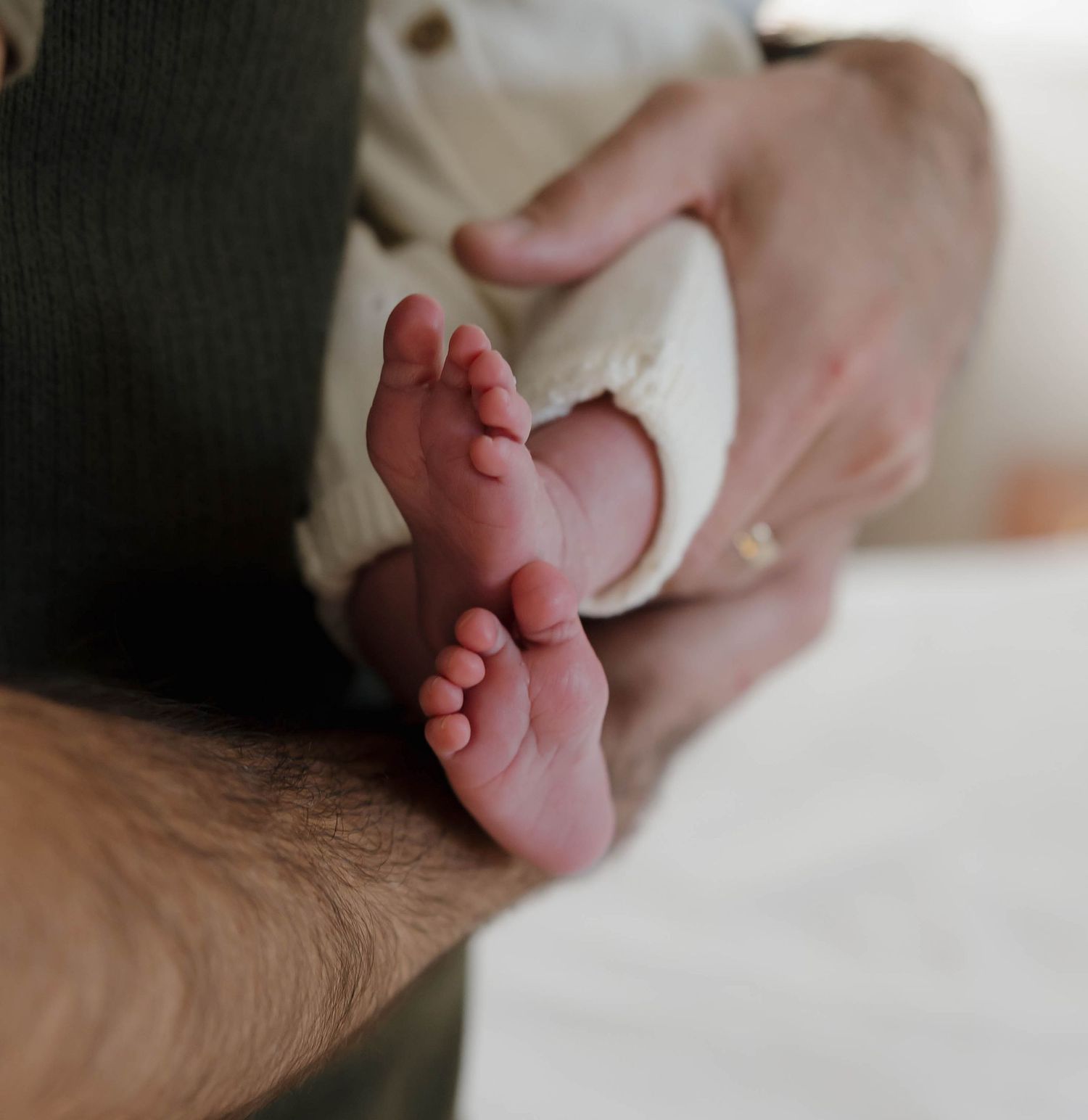 Delicate newborn baby toes and feet resting on soft white fabric in natural light.