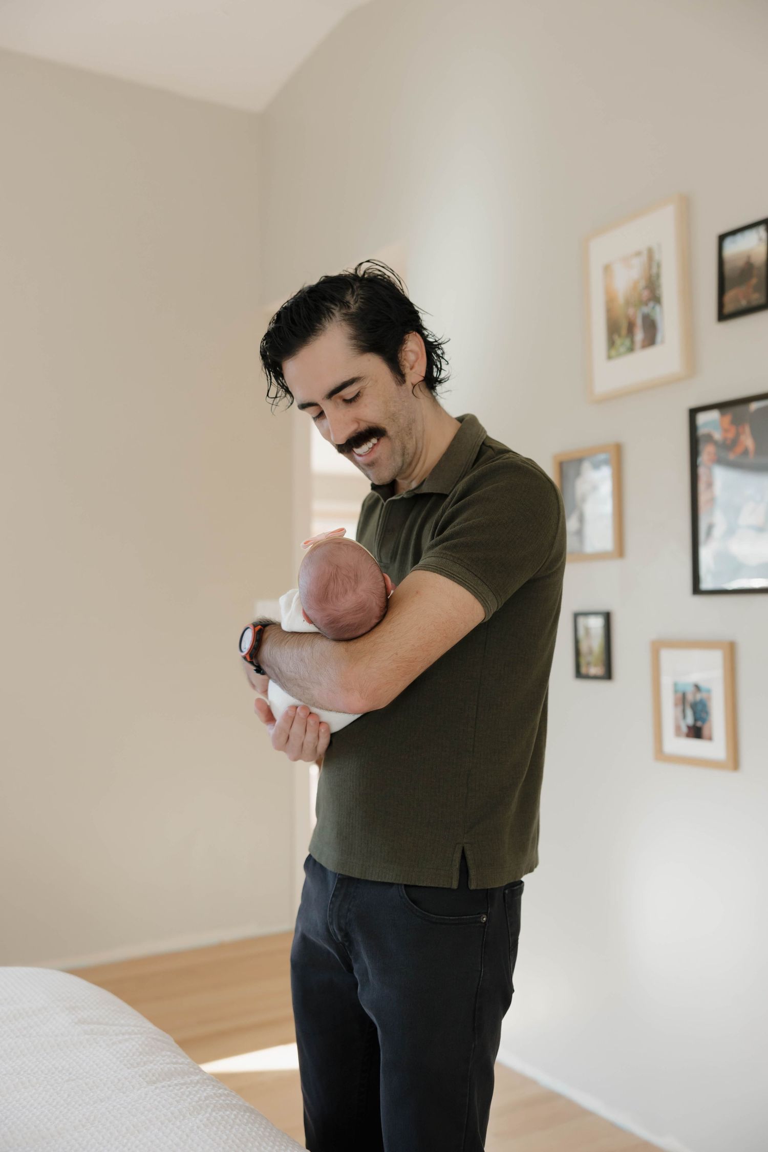 A series of tender moments showing a parent holding and comforting a small baby in a room with framed photos.