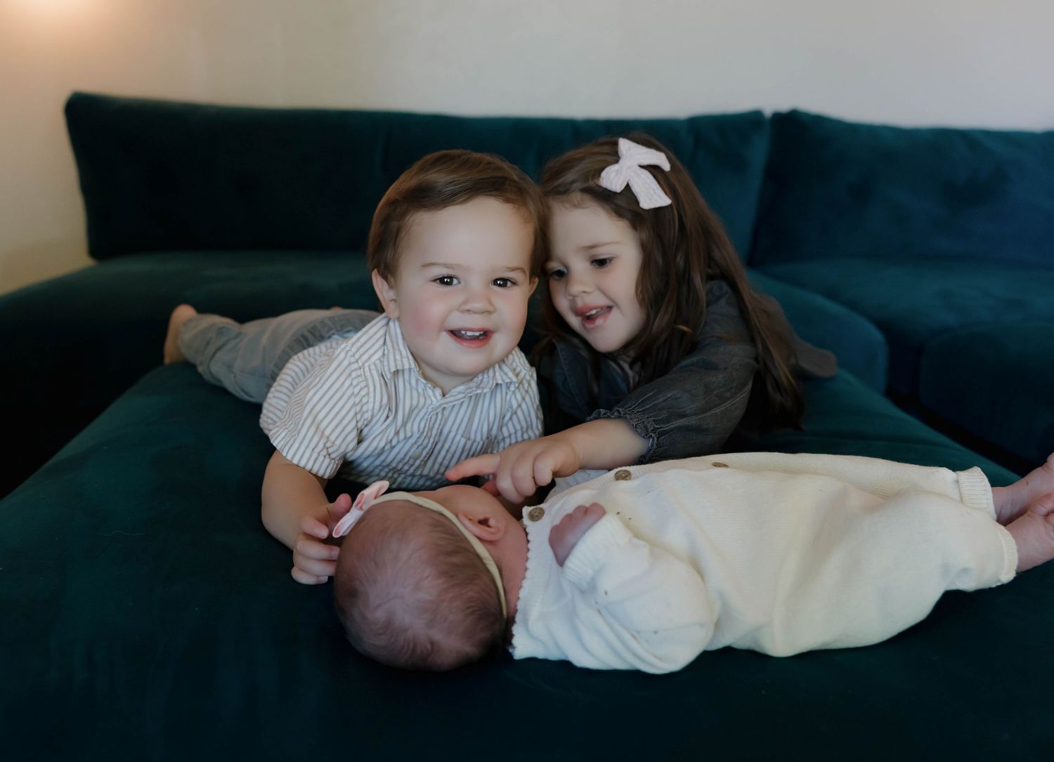 Children sitting together on a dark teal couch sharing a sweet moment with a baby.