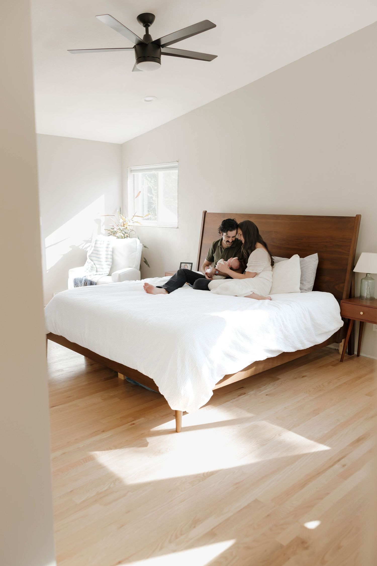 Bright and airy bedroom with white bedding, wooden headboard, light hardwood floors, and natural sunlight streaming in.