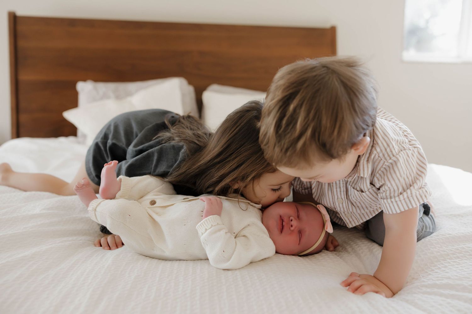 Sweet newborn baby resting peacefully on white bedding in soft natural window light.