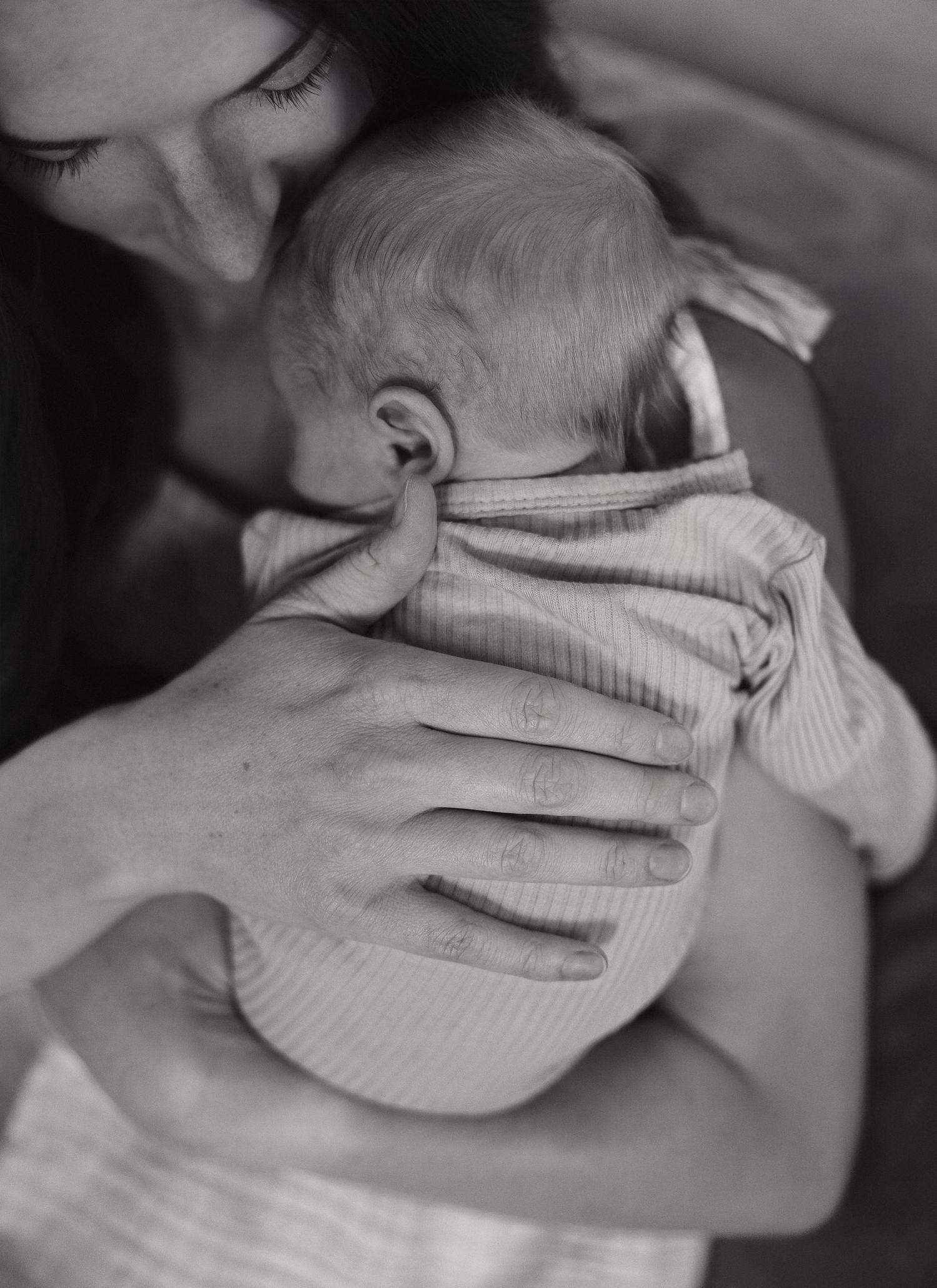 A tender black and white photograph shows hands gently cradling a baby wearing a striped onesie.