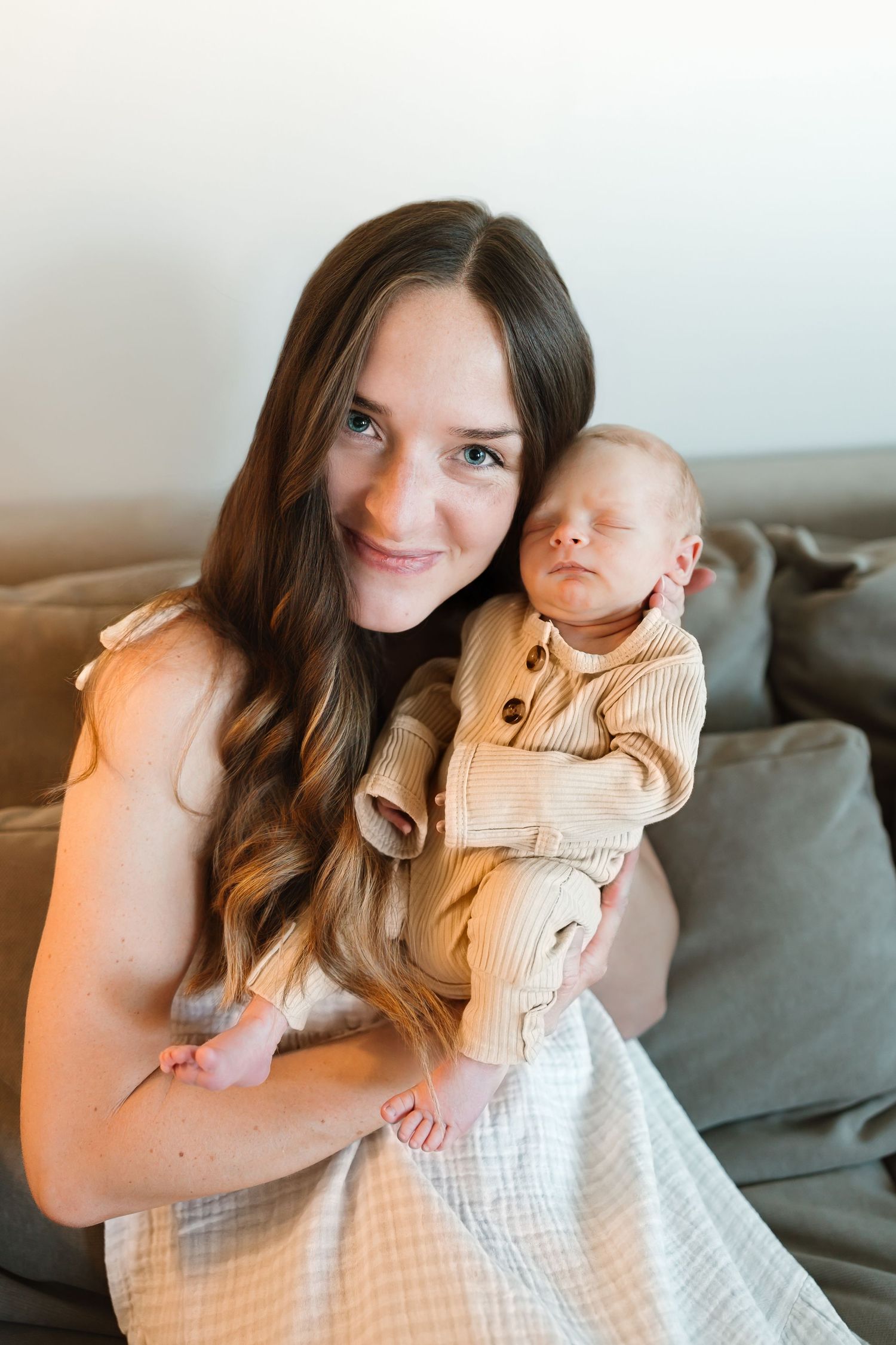 A mother and baby share tender moments while sitting together on a gray couch in a series of candid photos.