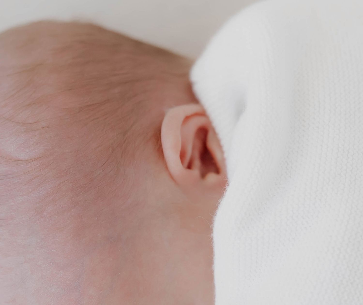 Close-up view of a baby's ear against a soft white background.