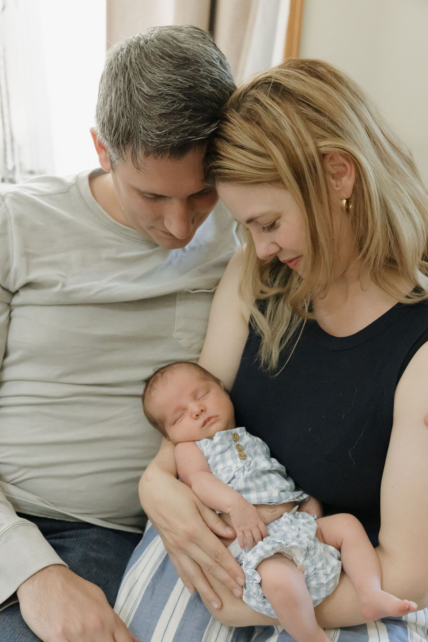 A tender moment as parents cradle their newborn baby wearing a blue checkered outfit.