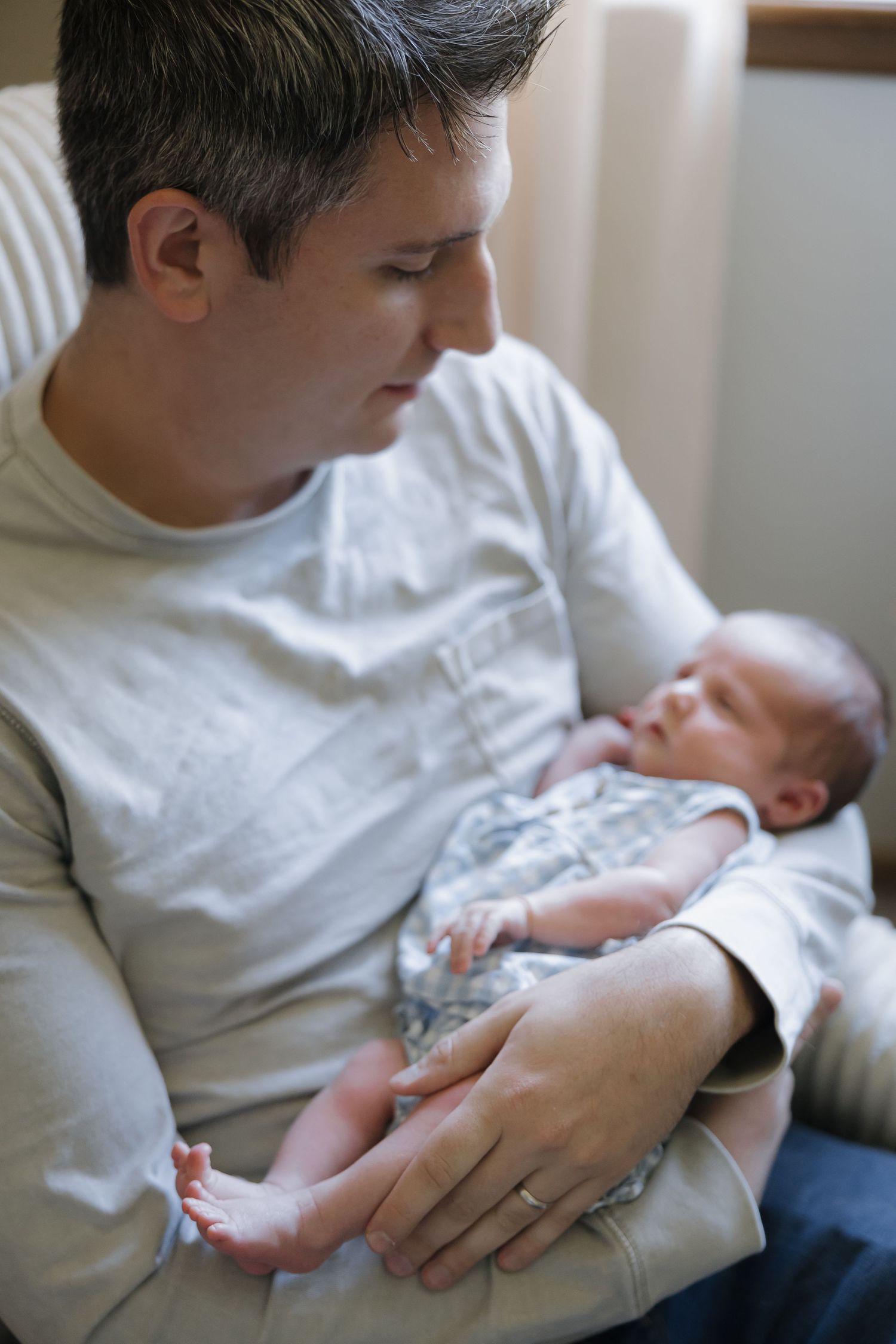 A tender moment as someone in a white shirt cradles a sleeping newborn baby in their arms.