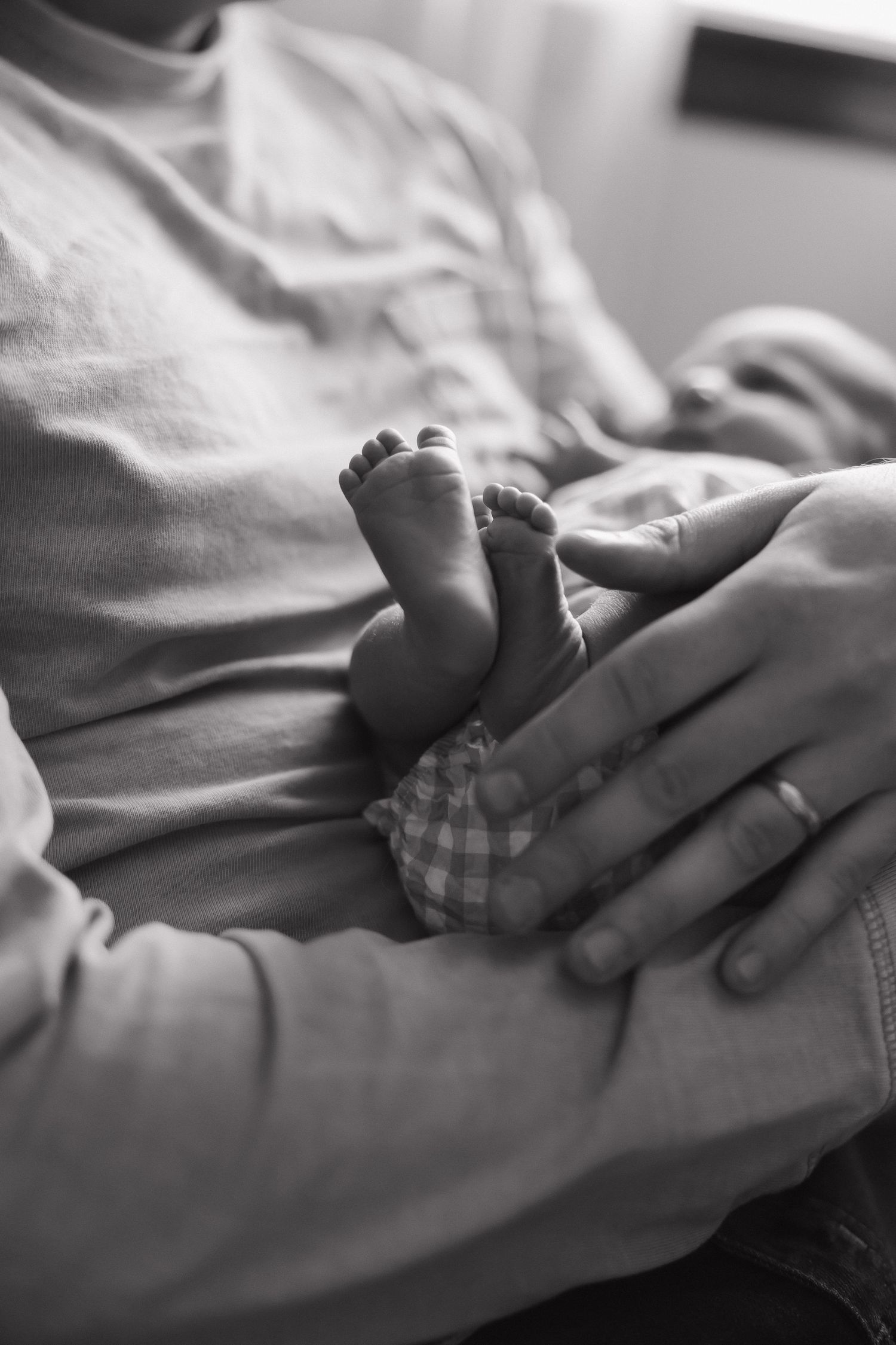 Close-up series of tiny baby feet being gently held against soft white fabric in black and white photography.