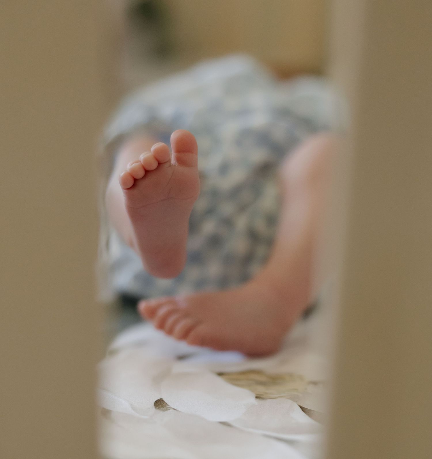 Close-up view of tiny newborn baby feet against white bedding showing delicate toes and soft skin texture.