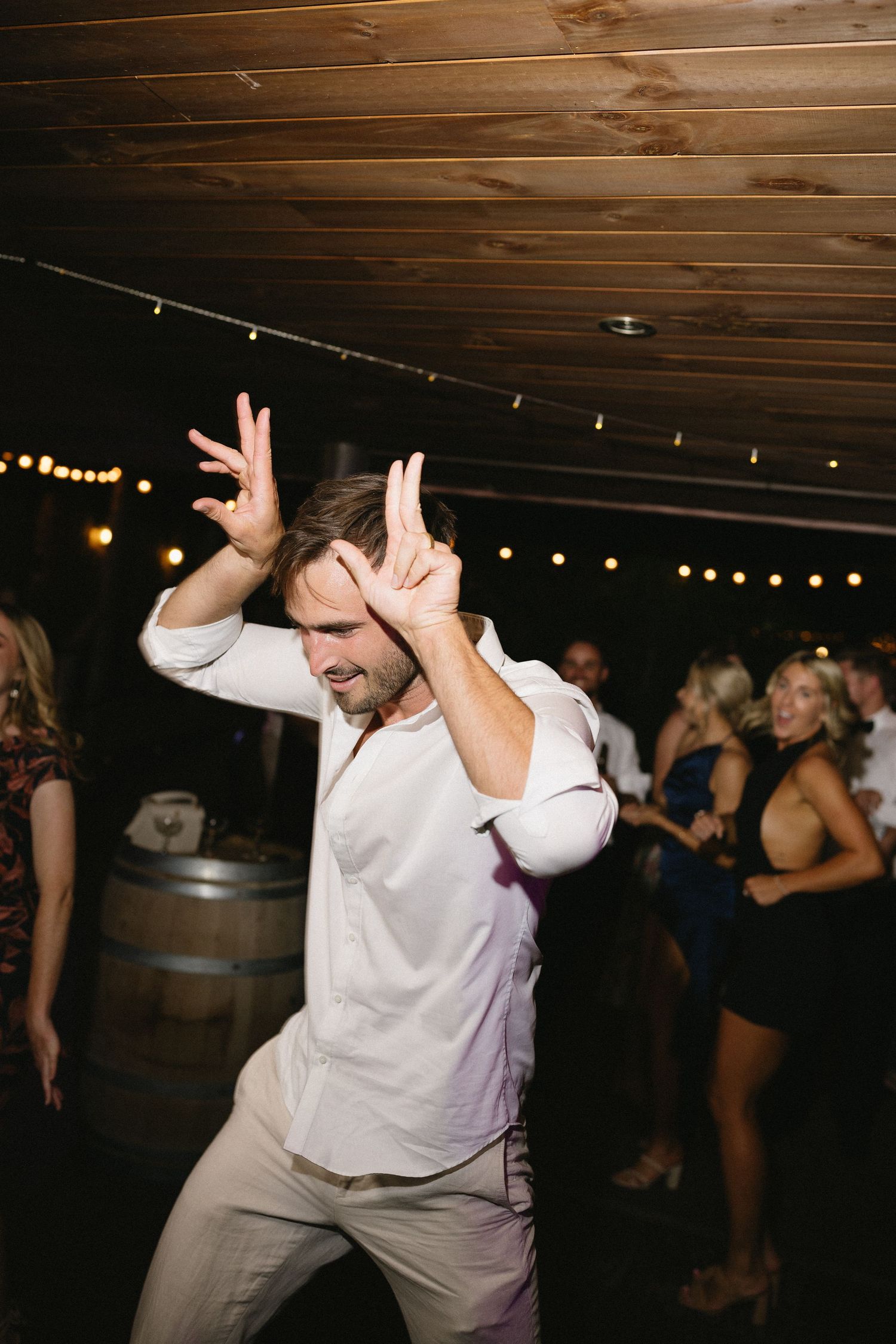 Wedding guest dances energetically under string lights at reception.