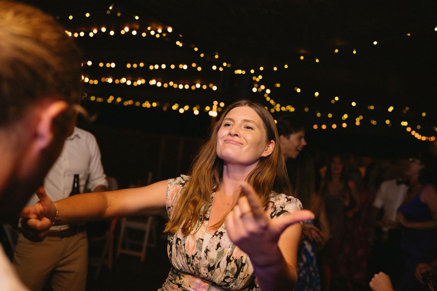 Guest dances joyfully under warm string lights at outdoor wedding reception.