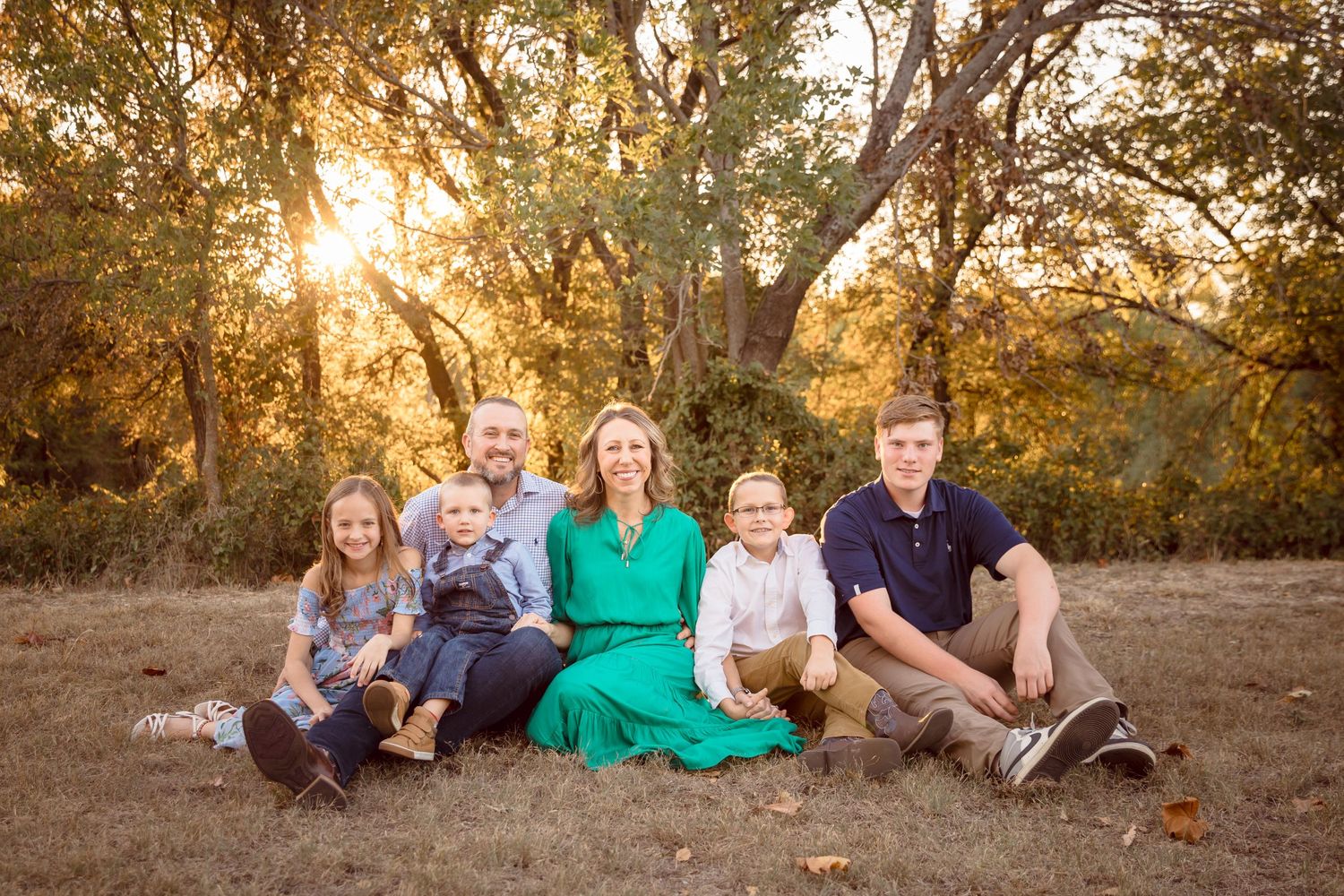 Family group relaxing on grass during golden hour photo session.
