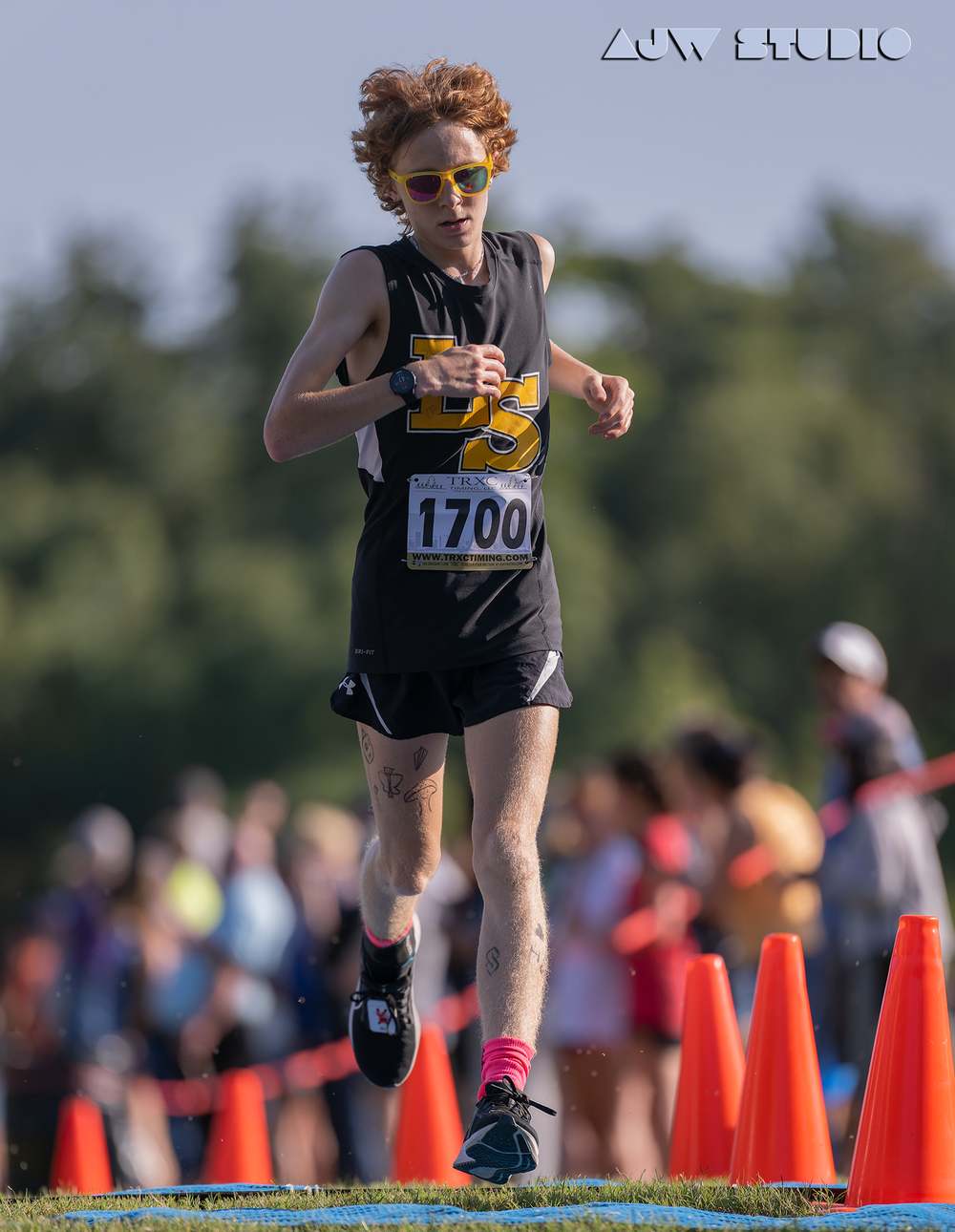 Runner wearing bib number 1700 navigates an outdoor cross country course marked with orange cones.