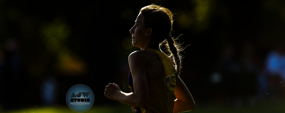 Cross country female runner captured in dramatic silhouette against sunlit backdrop.