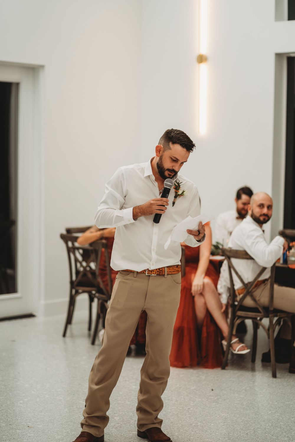 Wedding speech being given by a speaker in a white shirt and khaki pants at an indoor venue.