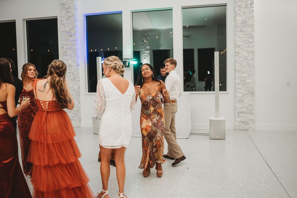 Wedding guests in colorful dresses socialize and dance at a modern reception venue.