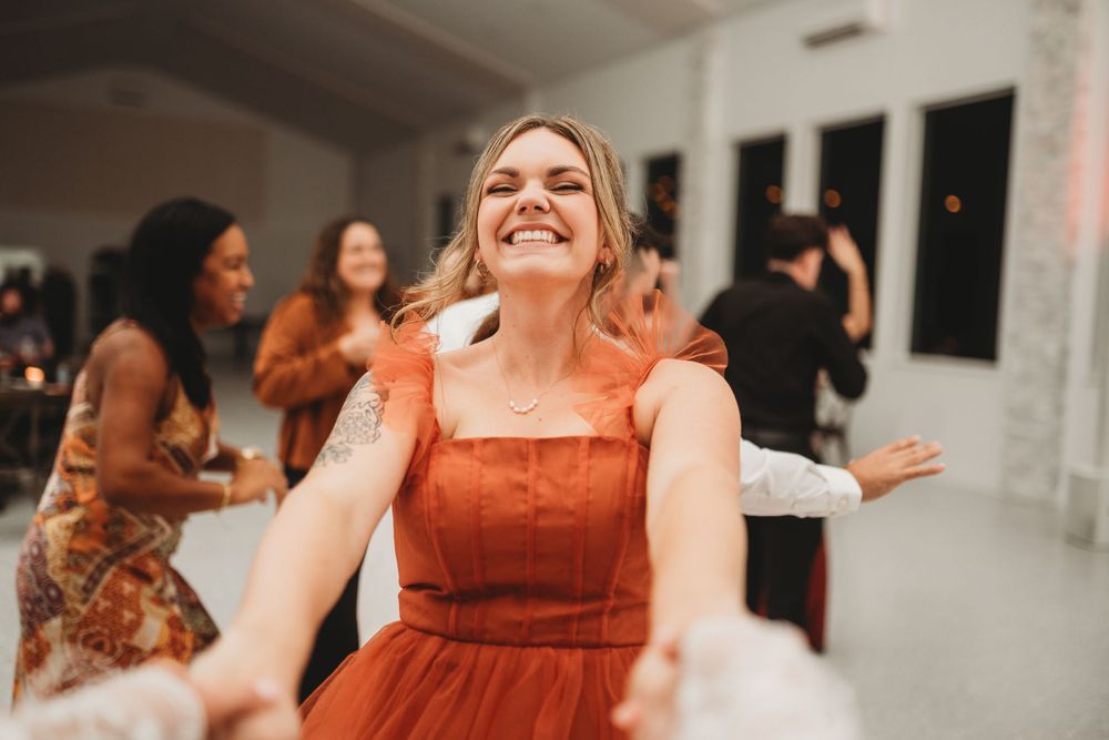 A guest in a rust-colored dress dances joyfully at a wedding reception.