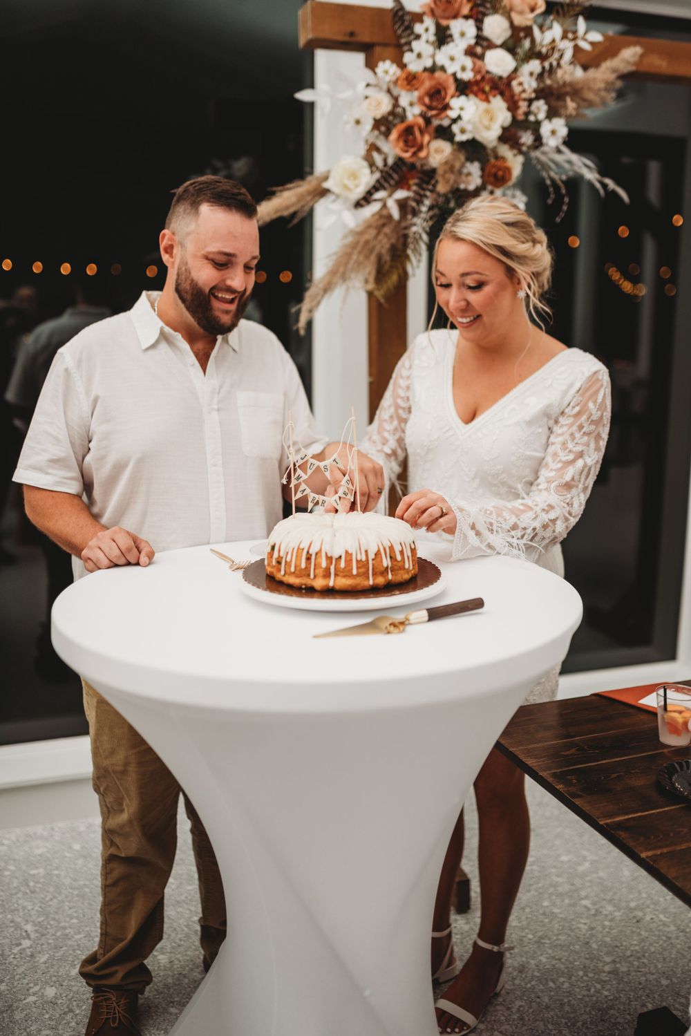 A couple cuts their bundt wedding cake at a modern reception decorated with dried florals.
