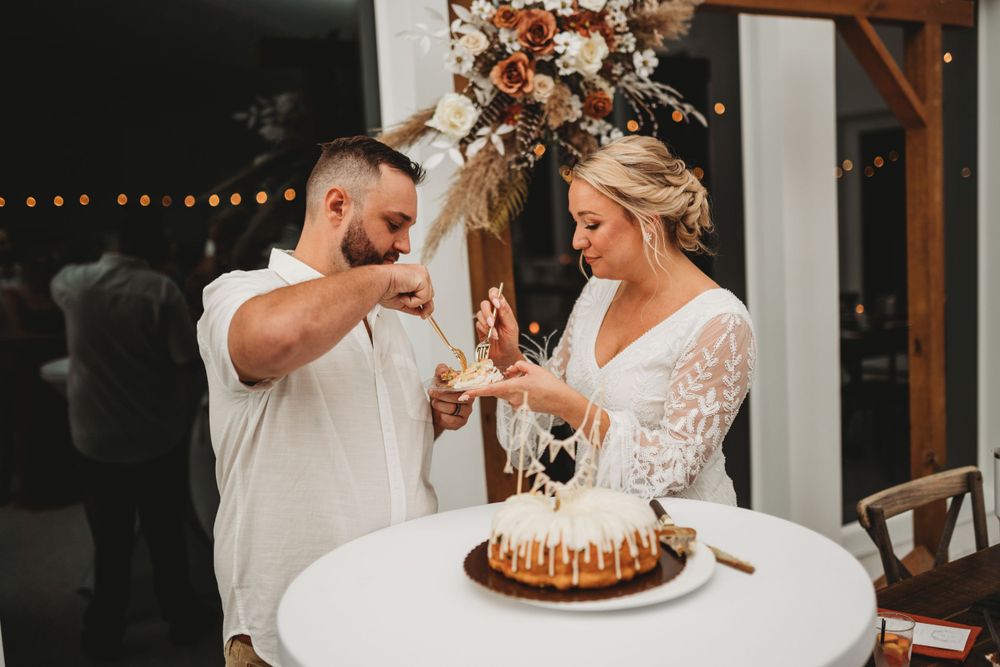 Couple laughing while feeding each other wedding cake at their reception.