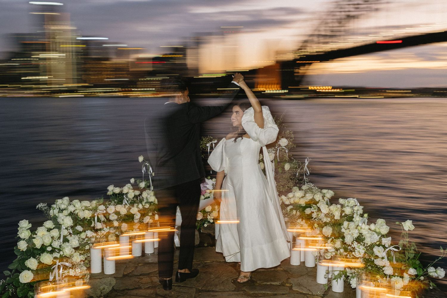Romantic outdoor wedding reception setup at sunset with glowing candles and white floral arrangements along the pathway.