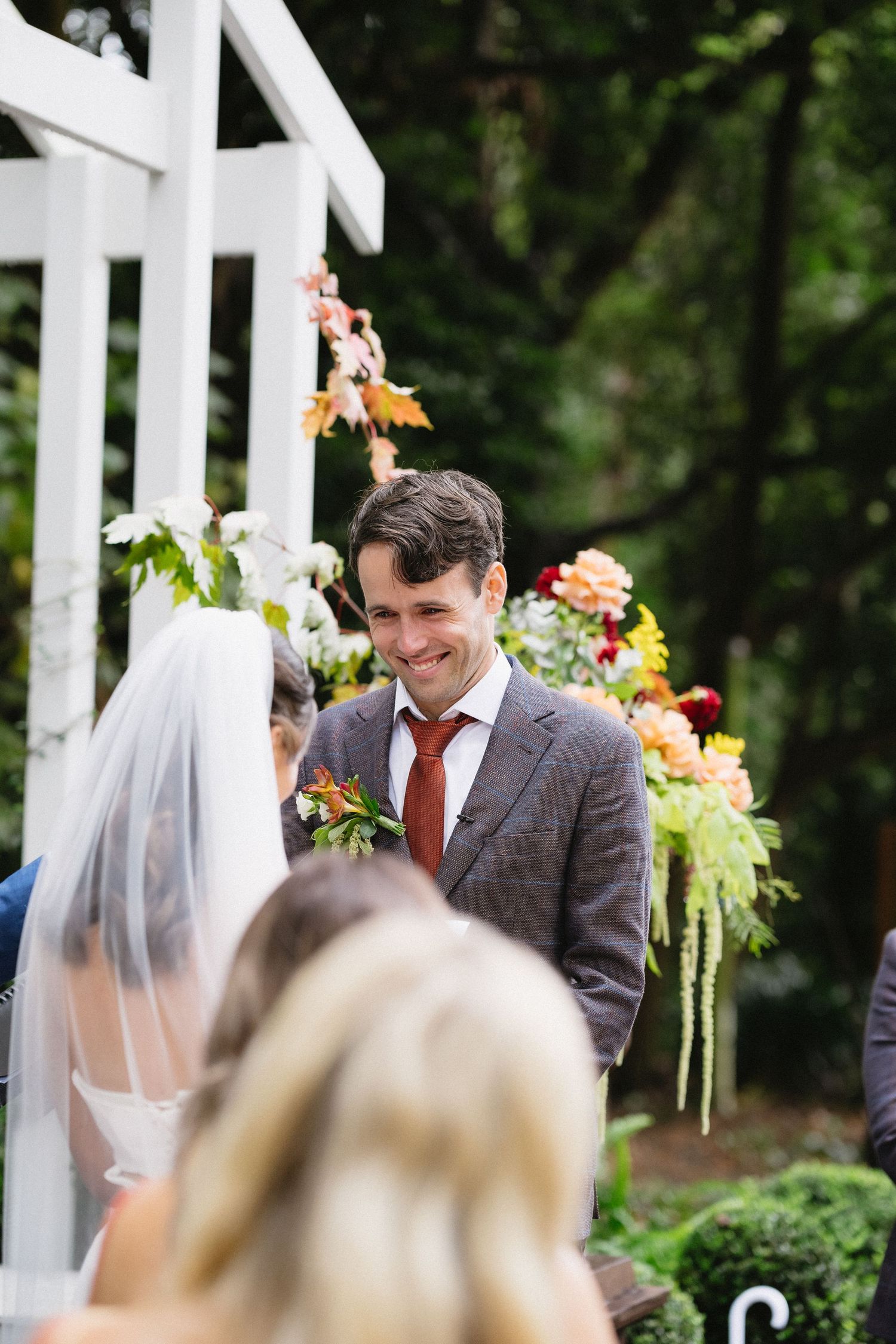 Garden wedding ceremony under a white pergola decorated with colorful floral arrangements.