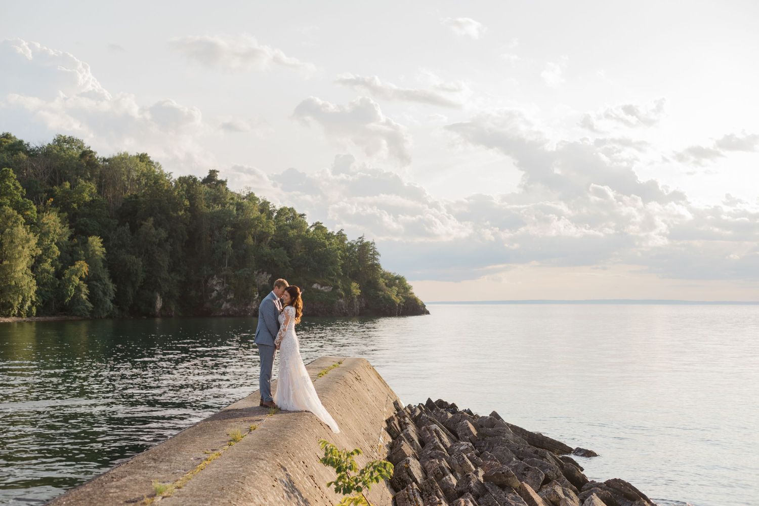Newlyweds share a romantic moment on a rocky shoreline at sunset.