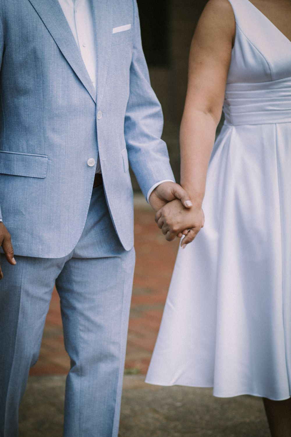 Close-up of a bride and groom holding hands, showcasing their wedding attire and photography by Empax Studios.