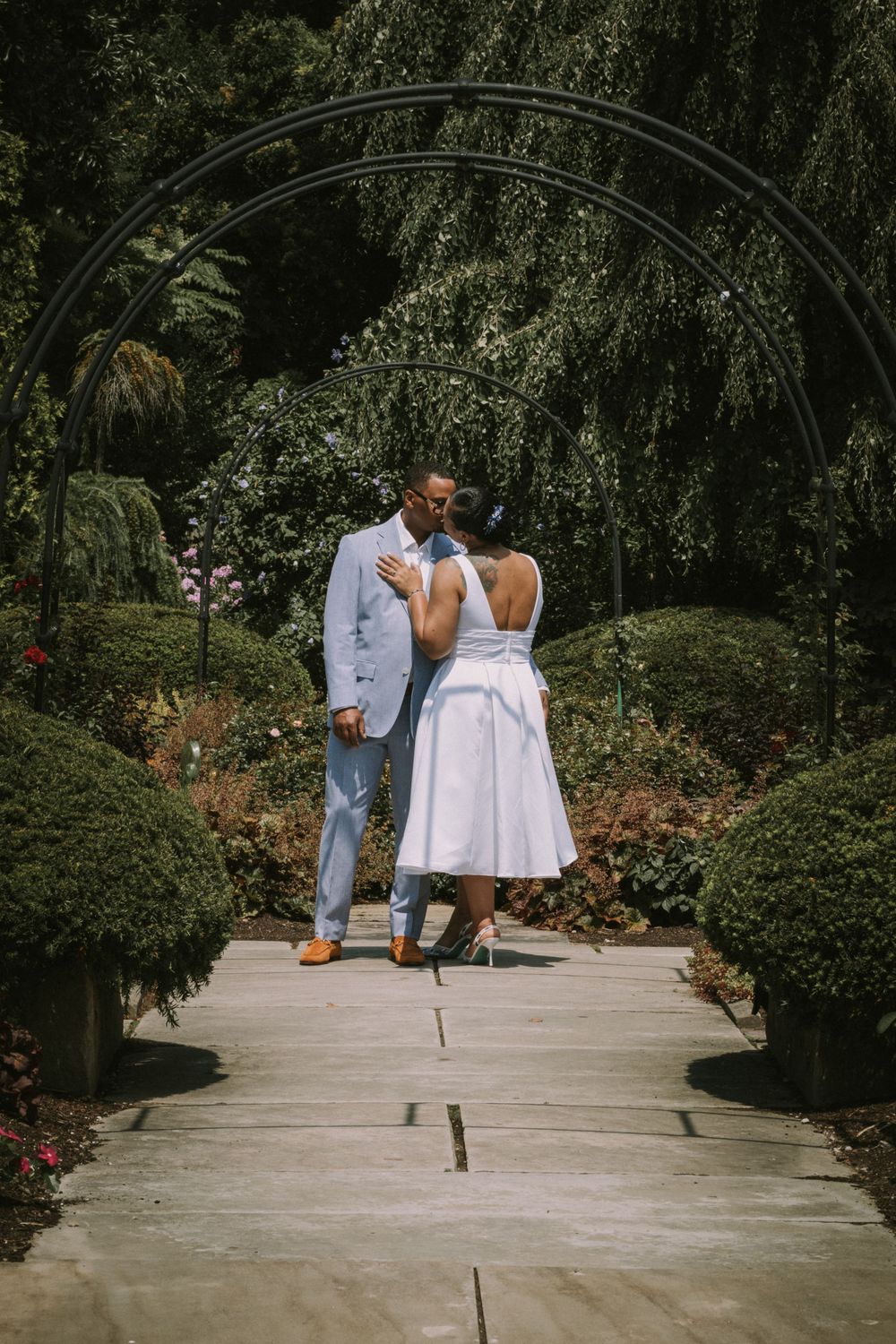 A magazine-style photo of a bride and groom standing under an archway in a lush garden, elegant wedding photography by Empax Studios