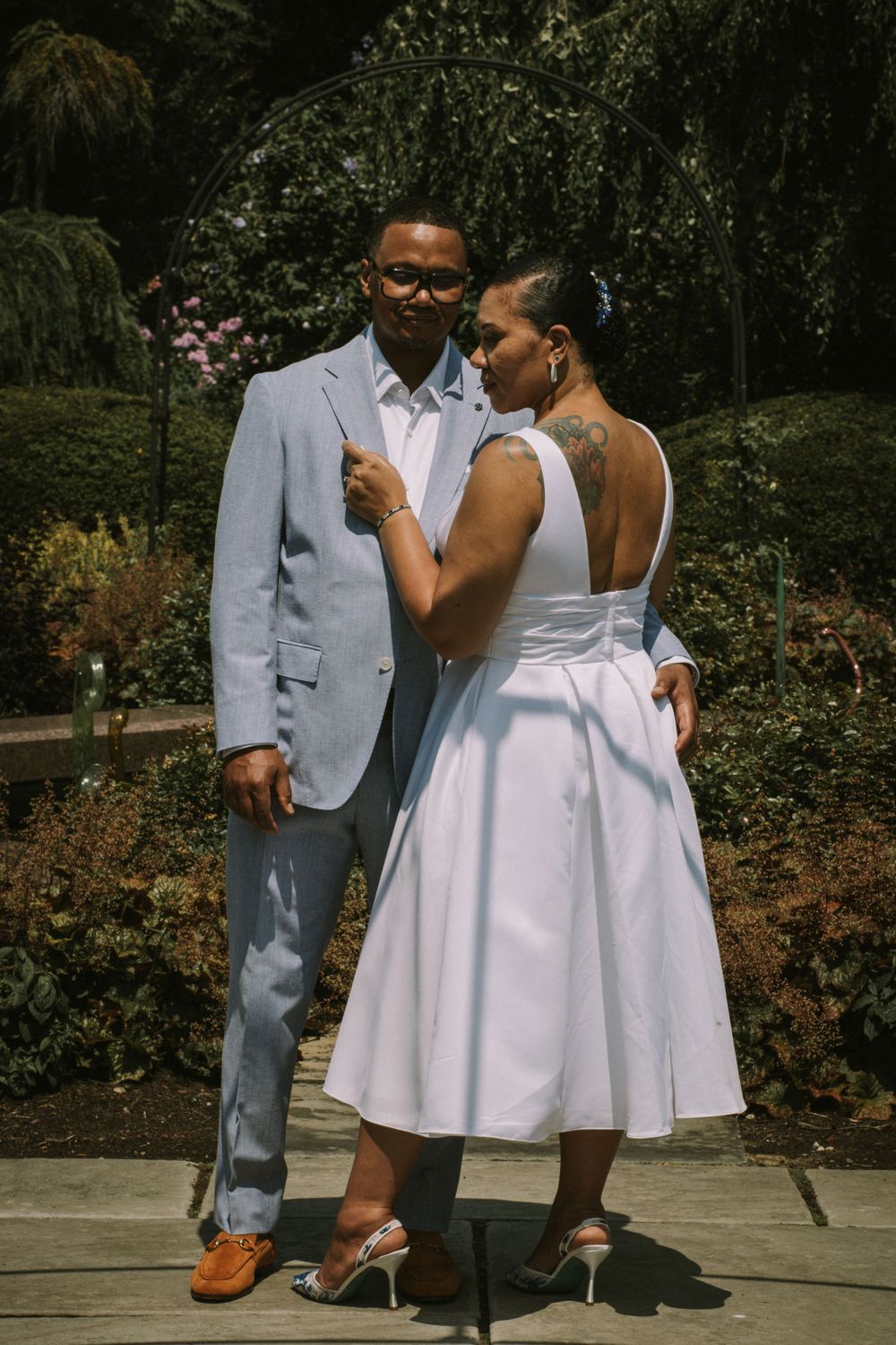 A bride and groom posing elegantly in a lush garden under an archway, showcasing magazine-style wedding photography by Empax Studios