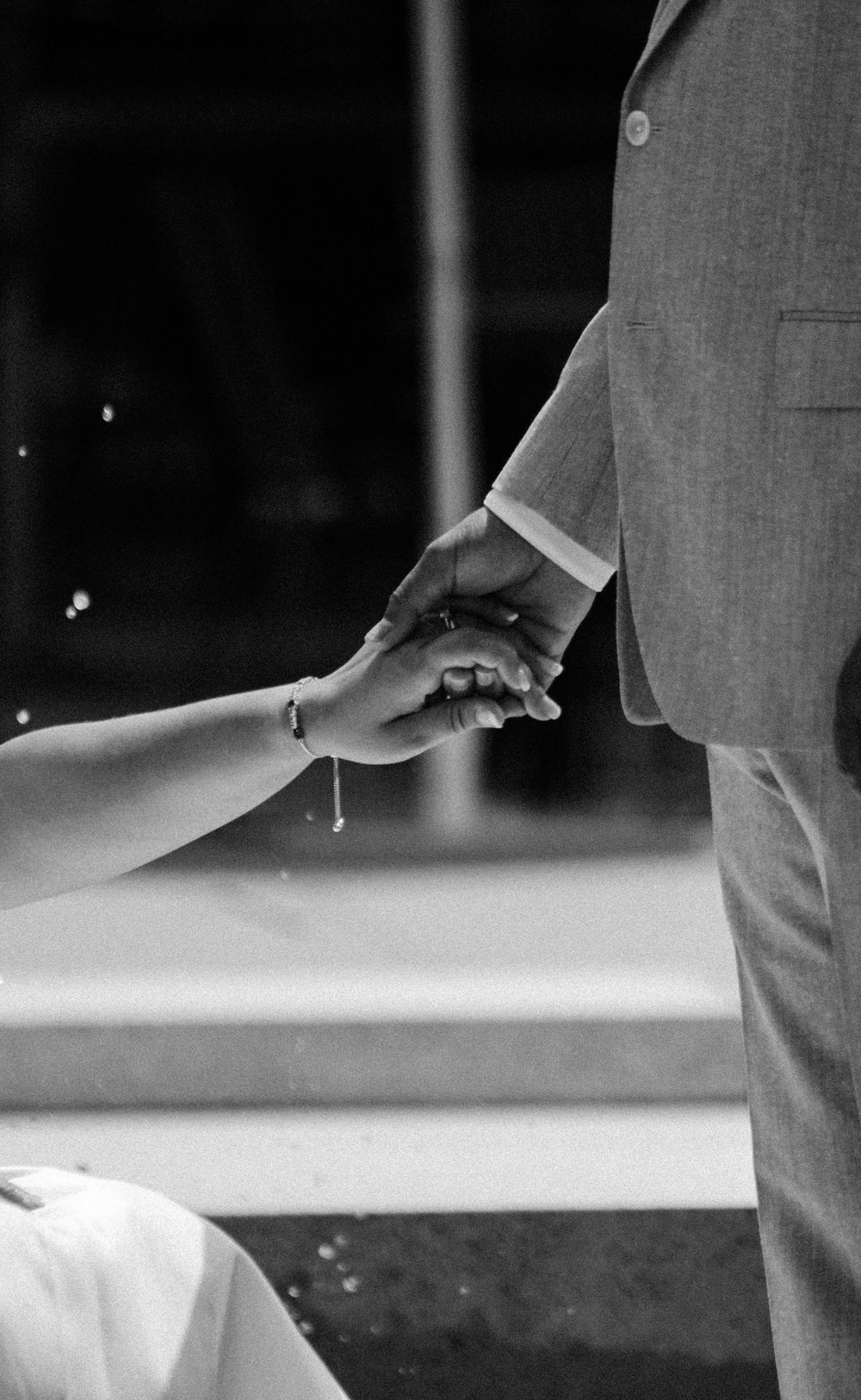 A black-and-white close-up of a bride and groom holding hands, symbolizing their connection, showcasing wedding photography by Empax Studios