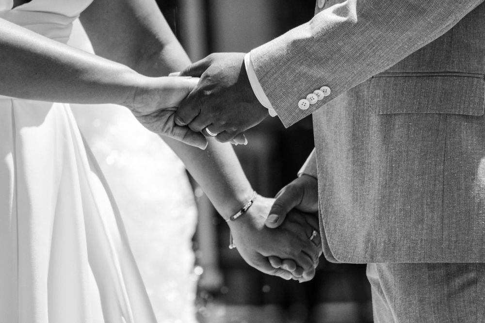 A black-and-white close-up of a bride and groom holding hands during their wedding ceremony, showcasing intimate wedding photography