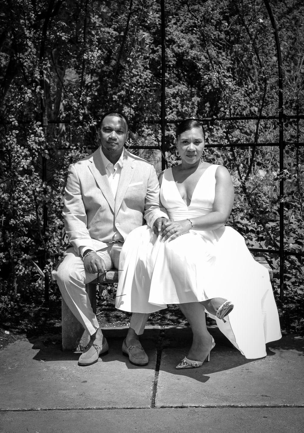 A black-and-white photo of a bride and groom seated together in a garden, showcasing timeless wedding photography by Empax Studios.