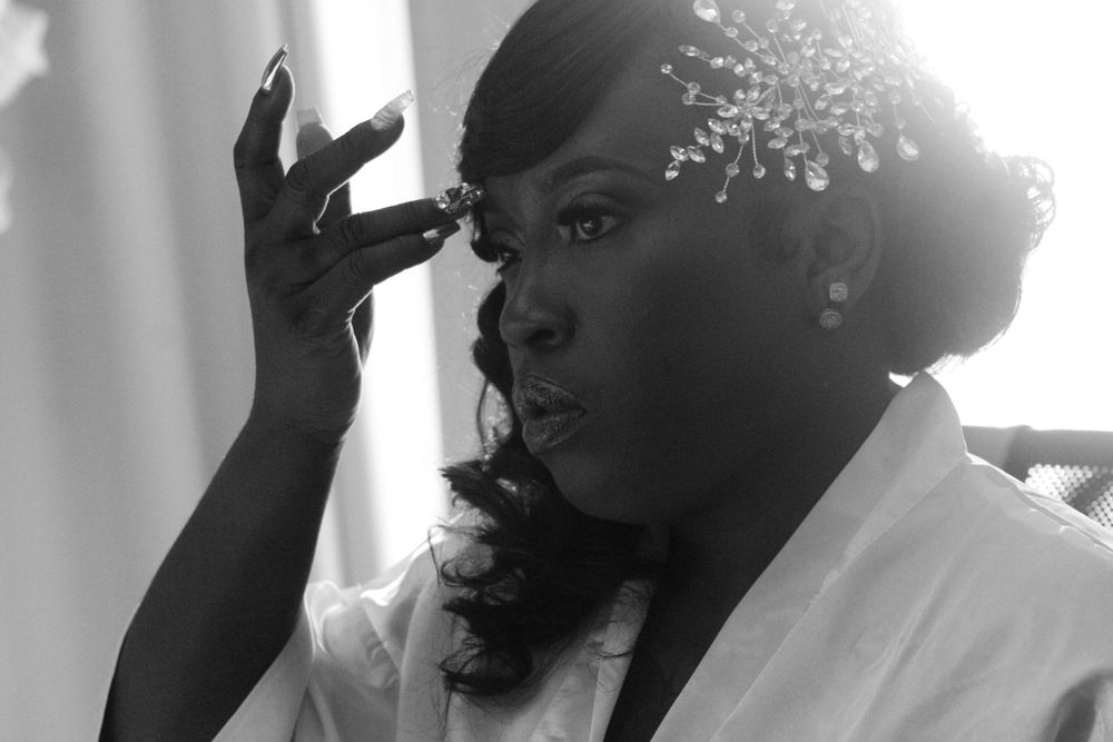 A black-and-white close-up of a bride adjusting her makeup while wearing a jeweled hairpiece, showcasing elegant wedding preparation photo