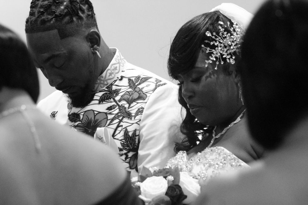 A black-and-white photo of a bride and groom bowing their heads in prayer during their wedding ceremony, showcasing intimate wedding photo
