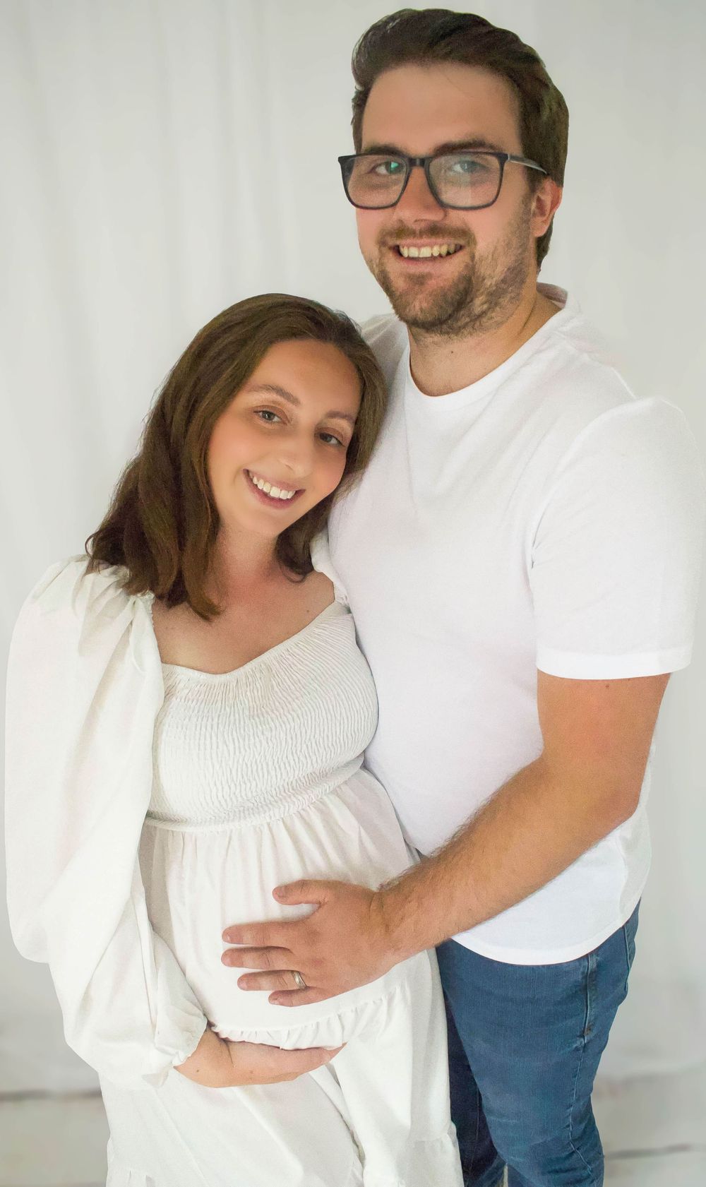 Expectant couple in white outfits pose together for maternity photo.