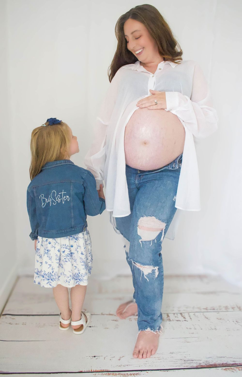 Mother and daughter share a special moment during maternity photoshoot in white studio setting.