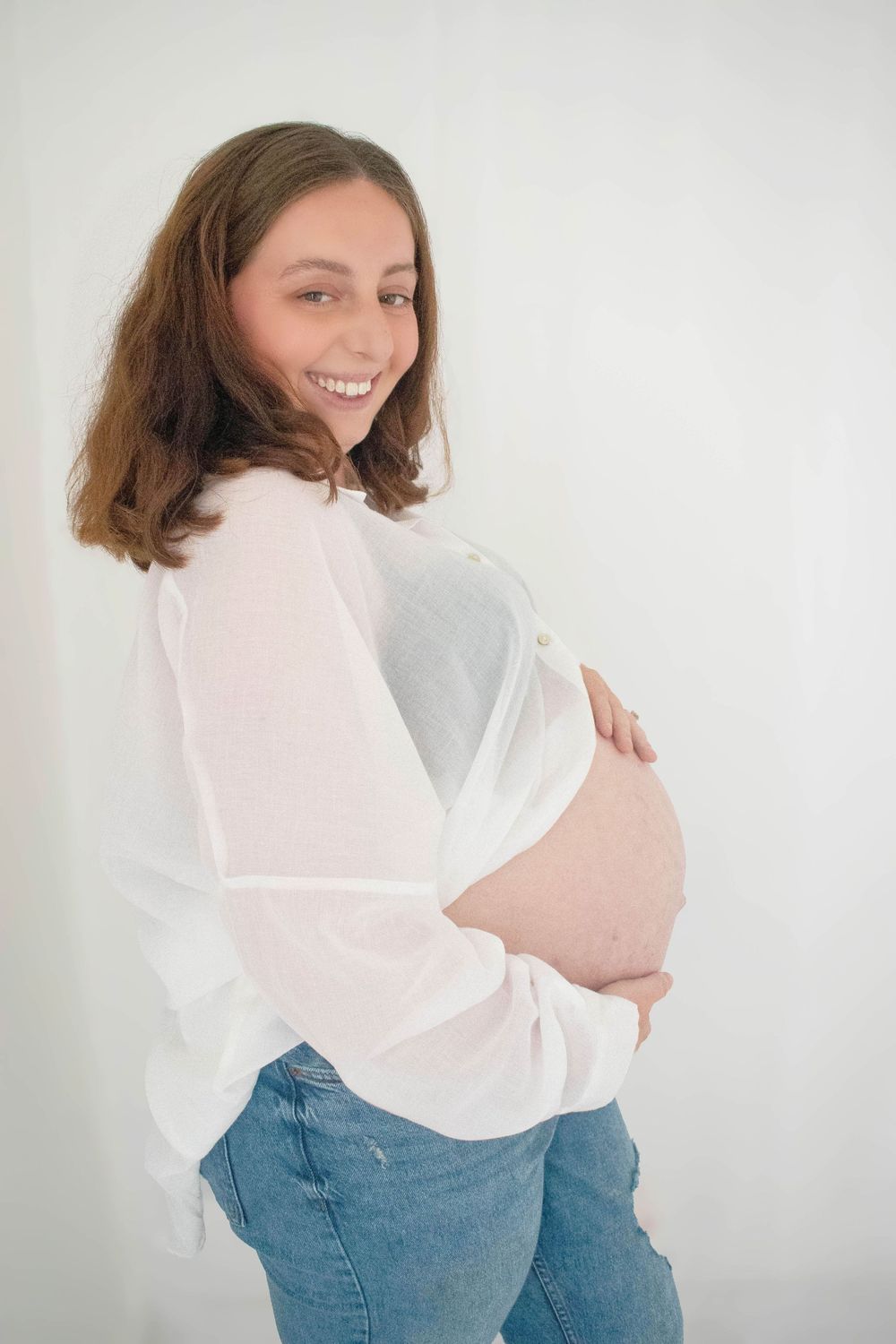 Woman in white top and jeans poses against white wall in casual lifestyle portraits.