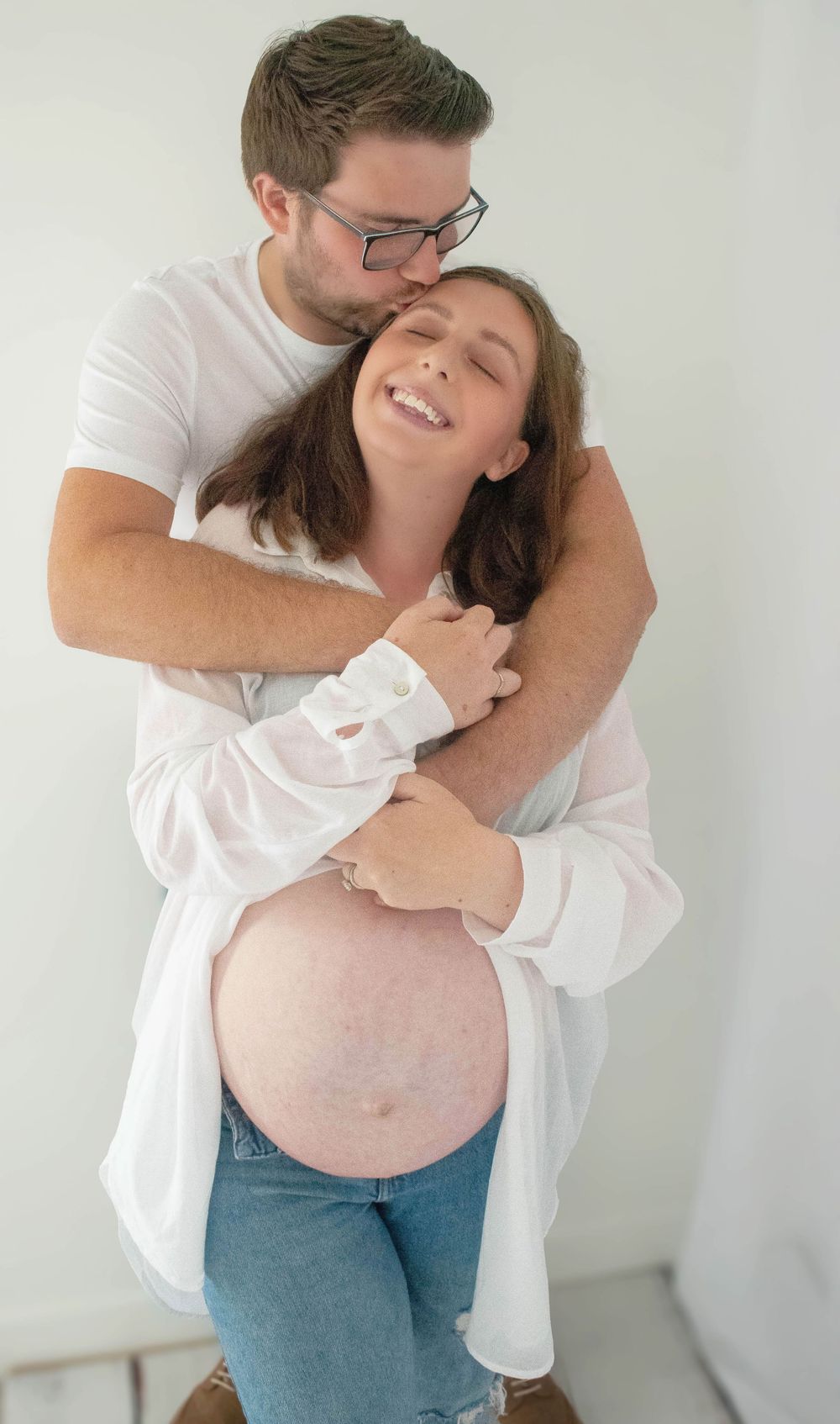 Intimate maternity photo of couple embracing against white background.