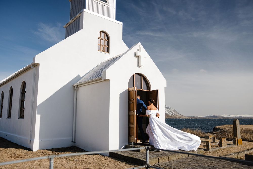 A white seaside church with flowing wedding dress in the doorway against blue skies.