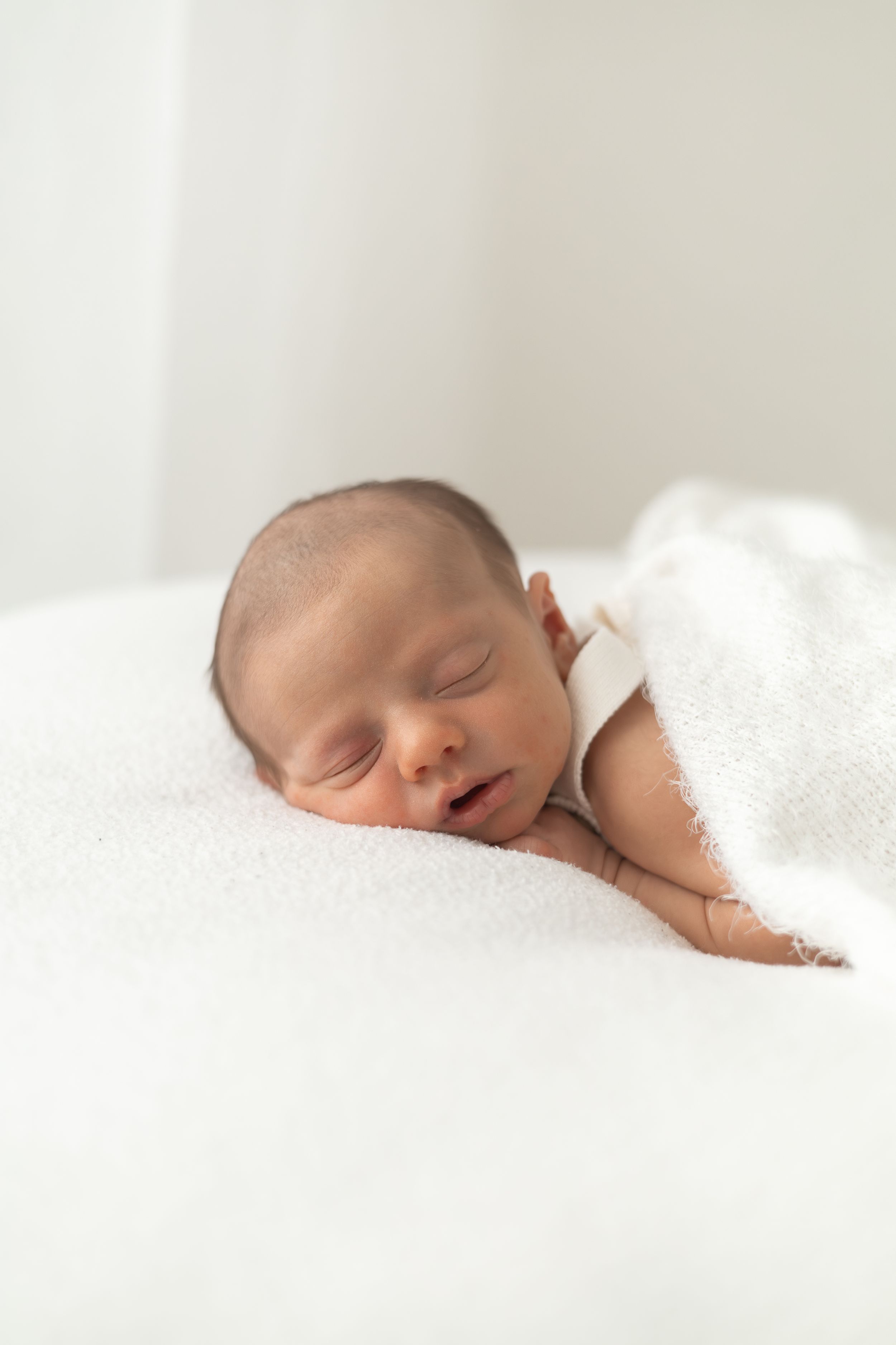 Peaceful newborn baby sleeping on a soft white blanket, gently wrapped in a white towel Nottingham newborn photographer