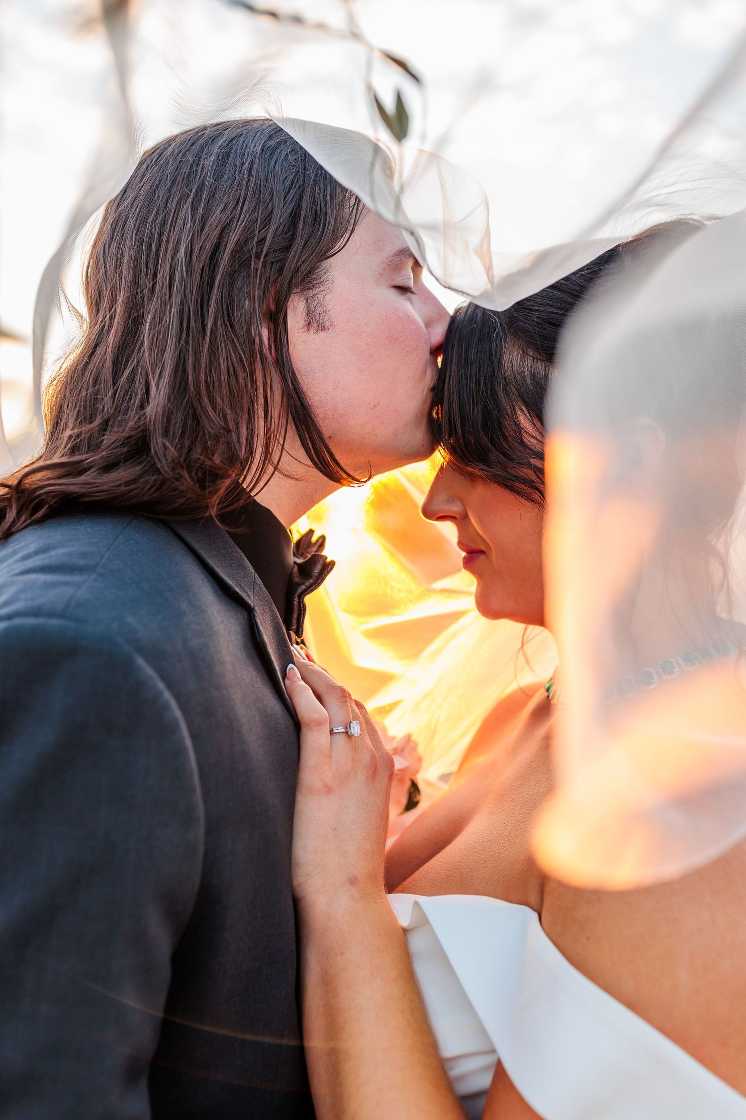 Romantic sunset kiss with golden light streaming through wedding veil.