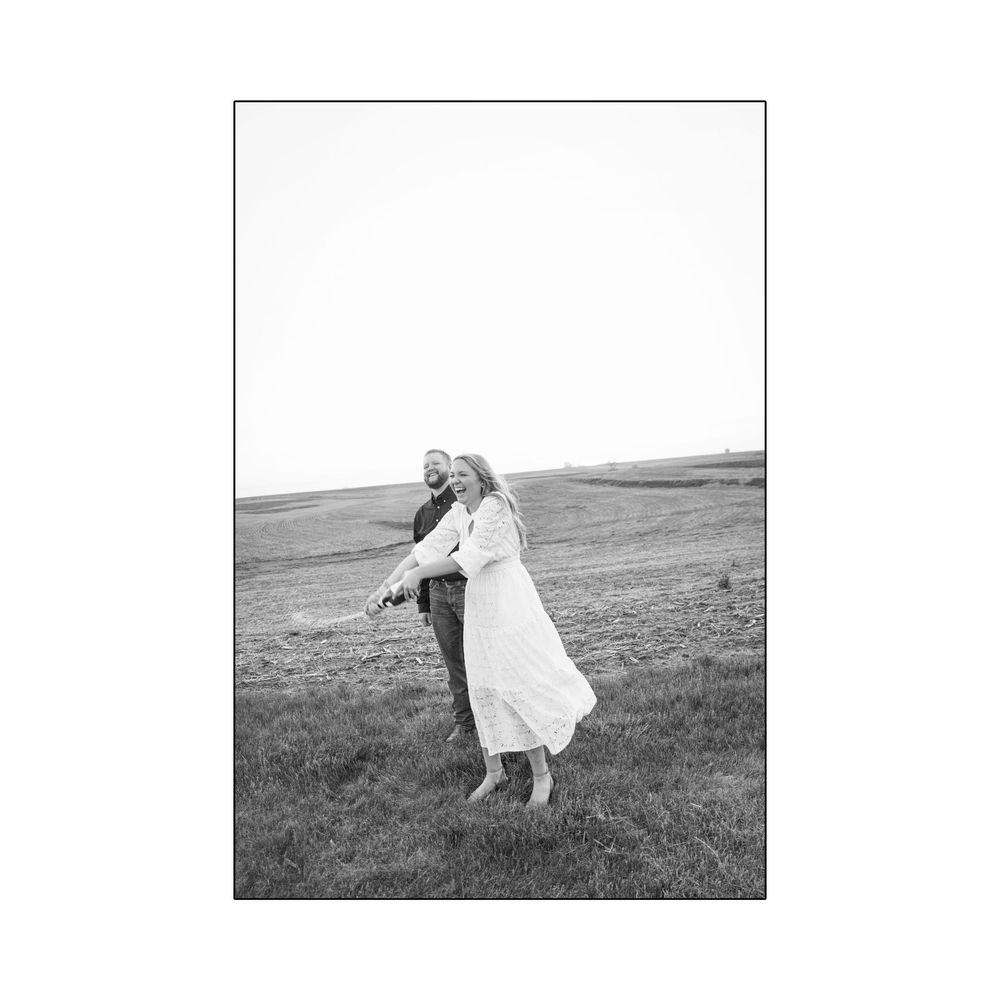 Black and white photo of a joyful couple spinning together in an open grassy field.