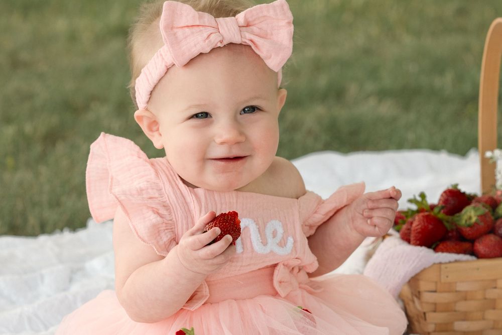Baby girl celebrating her first birthday outside with a pink strawberry shortcake milestone theme.