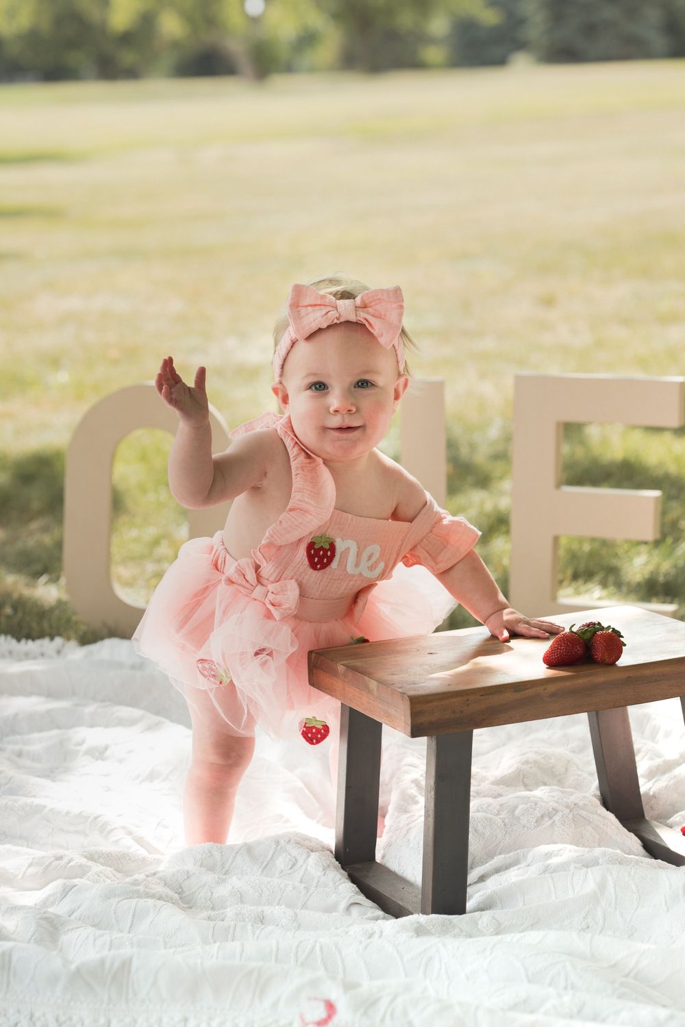 One-year-old girl standing outdoors in a pink dress during her first birthday portrait session.
