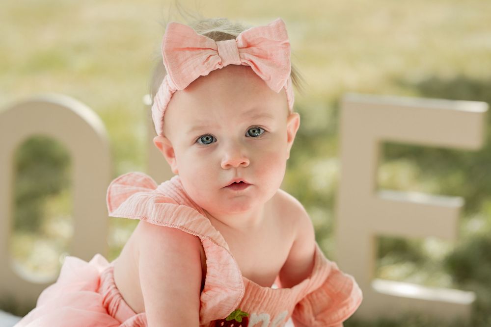 Close-up portrait of a one-year-old girl in a pink dress celebrating her first birthday outdoors.
