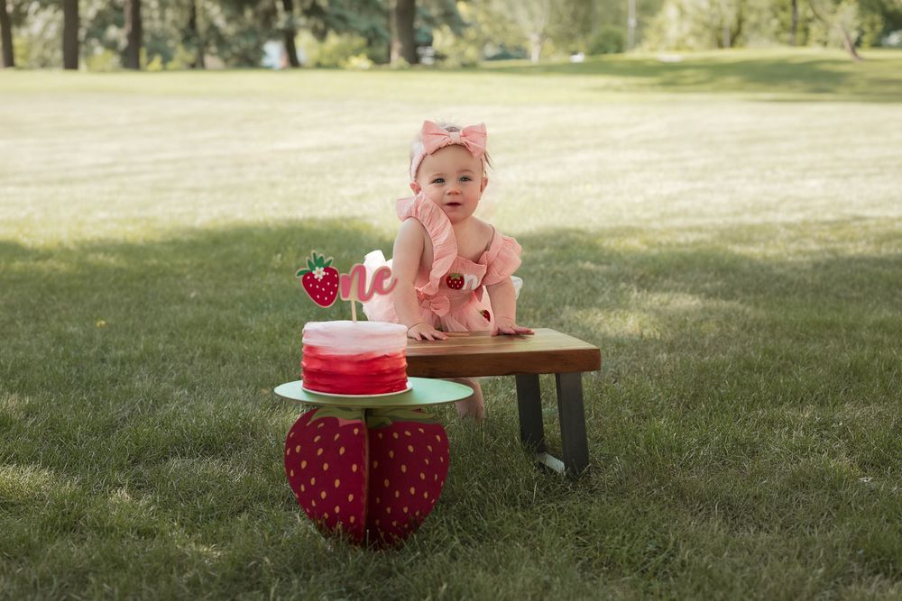 One-year-old girl laughing in a pink dress during her strawberry-themed birthday photoshoot.