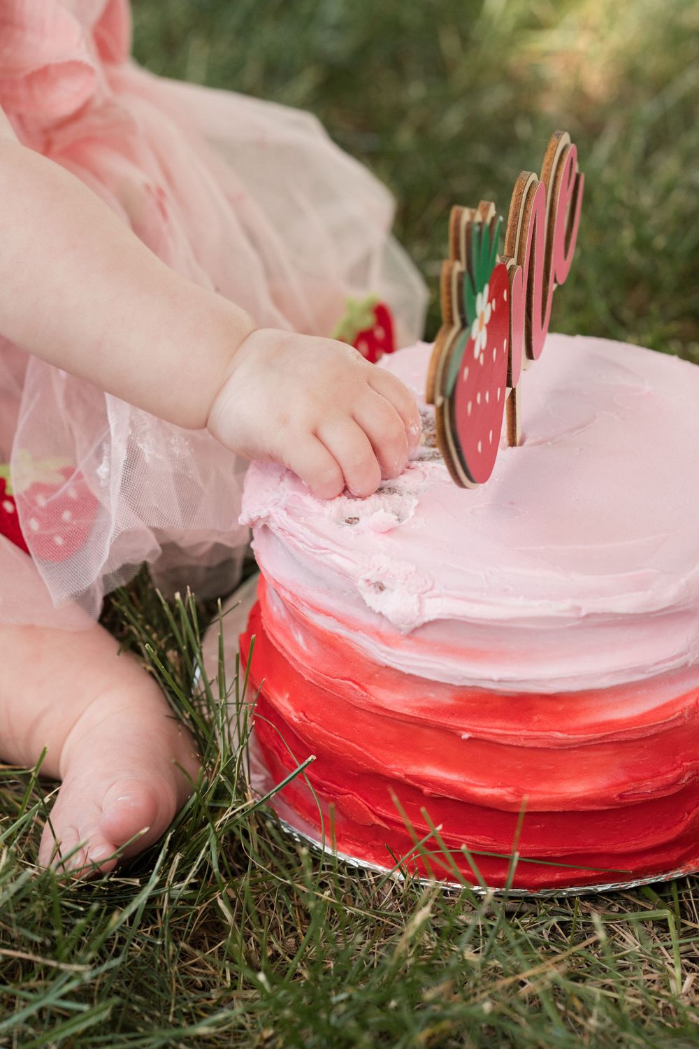 Close up image of strawberry shortcake cake and little girl fingers picking at frosting.
