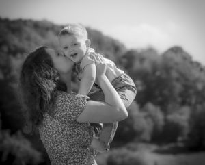 Black and white photo of joyful mother lifting laughing baby boy up in the air outdoors.