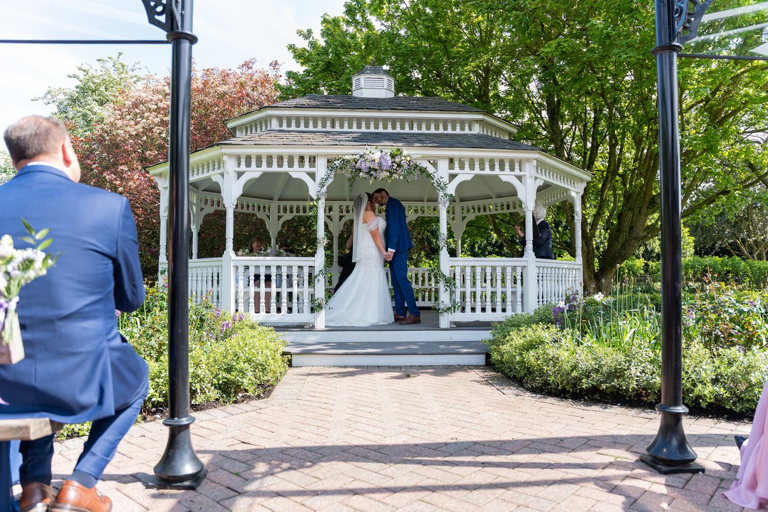 Bride and groom exchange vows under a white gazebo surrounded by lush greenery at an outdoor wedding ceremony.