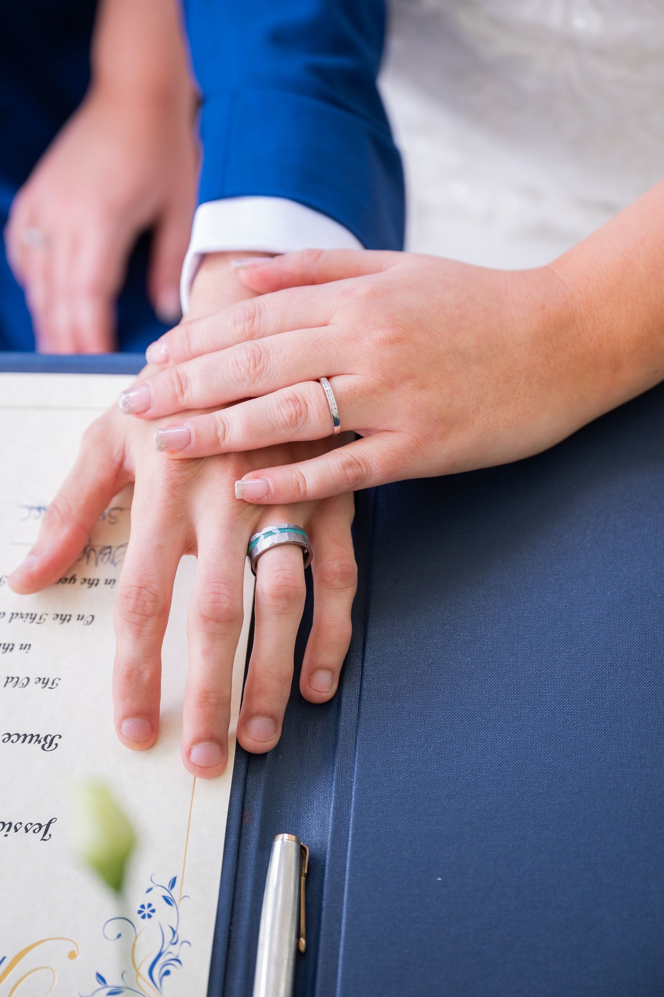 Newlyweds display wedding rings on hands resting on a marriage certificate with a pen nearby.